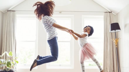 Mother and her daughter wearing a tutu jump in their living room