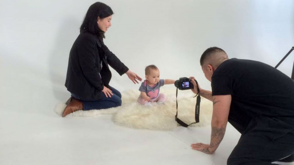 A baby being photographed by a photographer and has her mom by her side