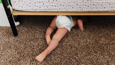 Small child in diaper crawling under bed