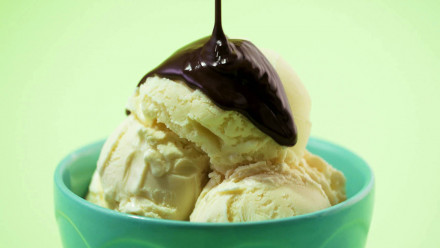 Three scoops of vanilla ice cream being topped with dark chocolate ganache