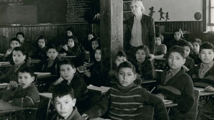 Photo: Cree students at their desks with their teacher in a classroom, All Saints Indian Residential School, Lac La Ronge, Saskatchewan, March 1945