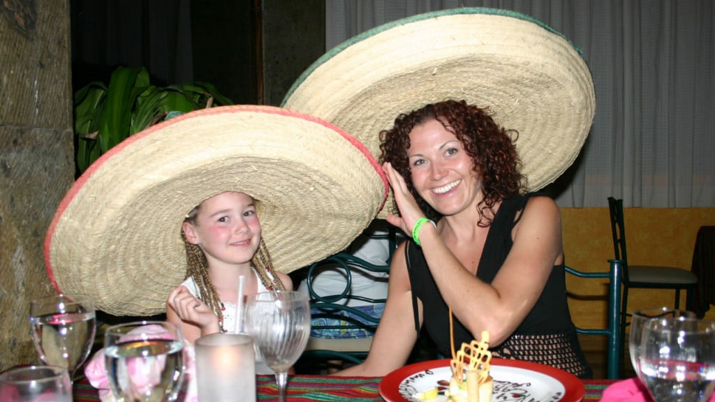 A woman sitting with her young daughter at a Mexican restaurant wearing Mexican hats.