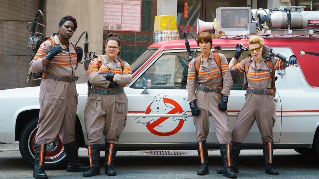 Proomo image for Ghostbusters showing the four women standing outside their car the Ecto-1