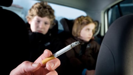 Kids in the backseat of a car with a cigarette in the foreground