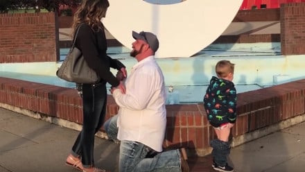 Man proposing to his girlfriend while a little kid stand behind him with his pants down