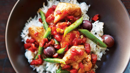 Bowl of chicken, green beans, tomatoes and olives over rice
