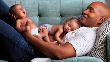 Dad laying on a couch holding his twin babies