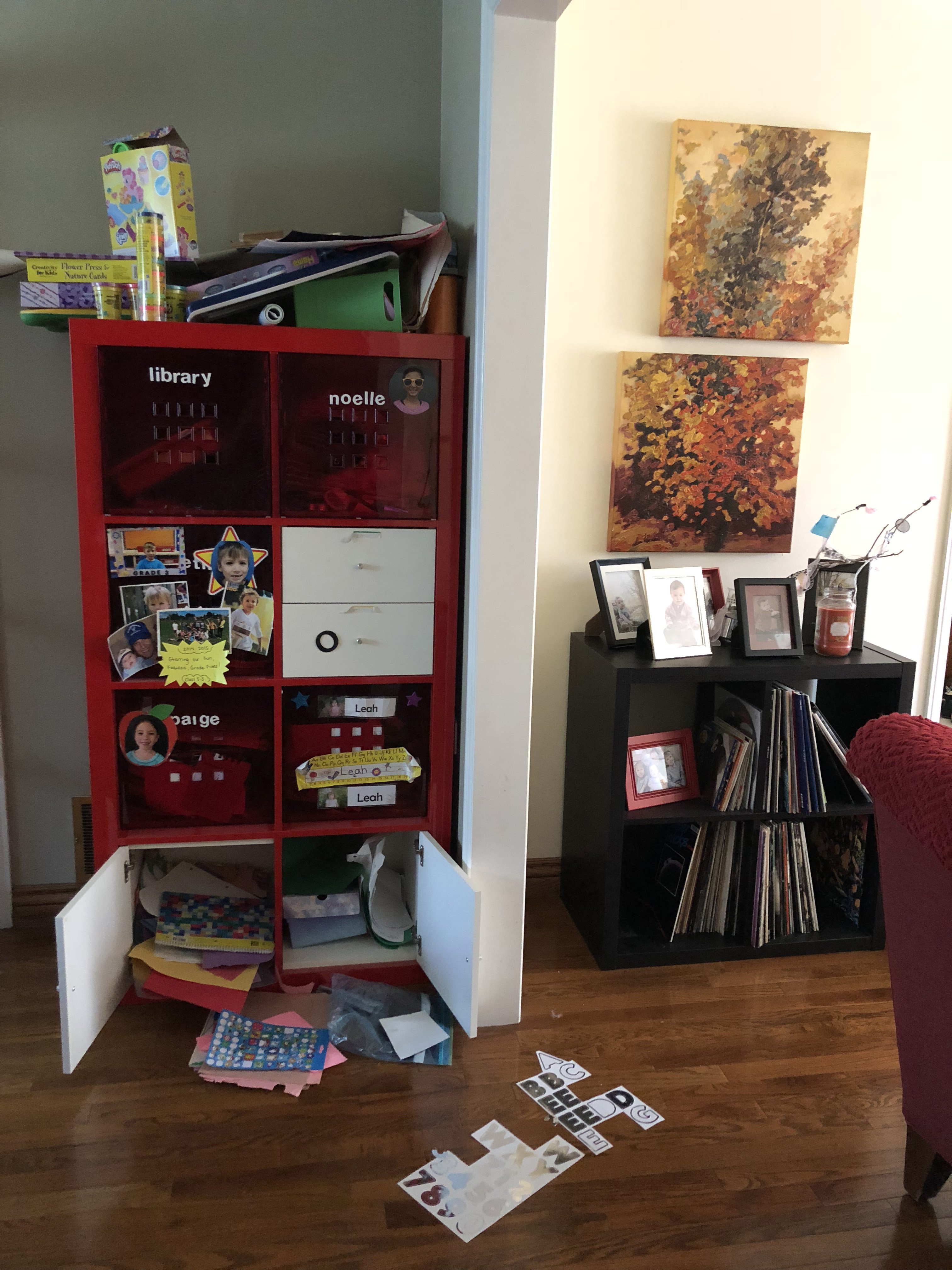 A picture of someone's living room with a bookcase overflowing with items falling out