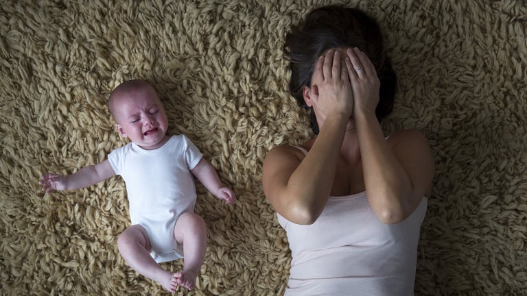 Mother and crying baby on a carpet while mother covers her face