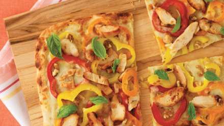 Flatbread pizza with slices of red and yellow and orange peppers with chicken and cheese