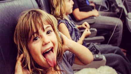 A little girl sticking her tongue out while listening to music on the an airplane