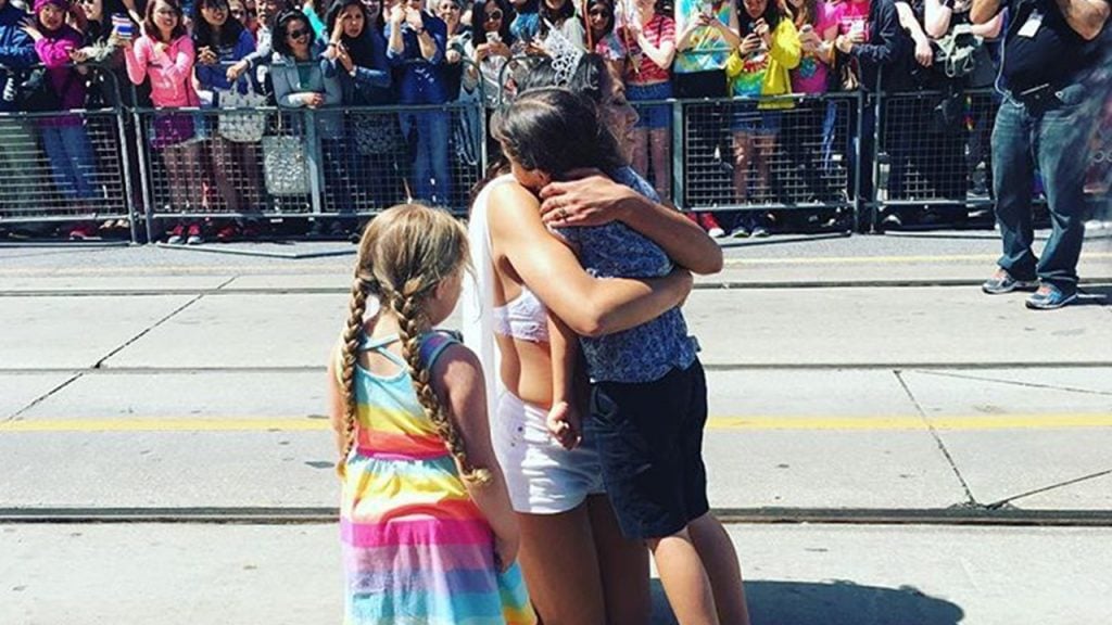A Drag queen at the pride parade hugs some kids in the street