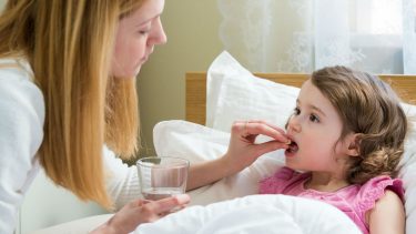 mother putting a pill in her daughters mouth