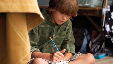 kid writing a letter home while at camp