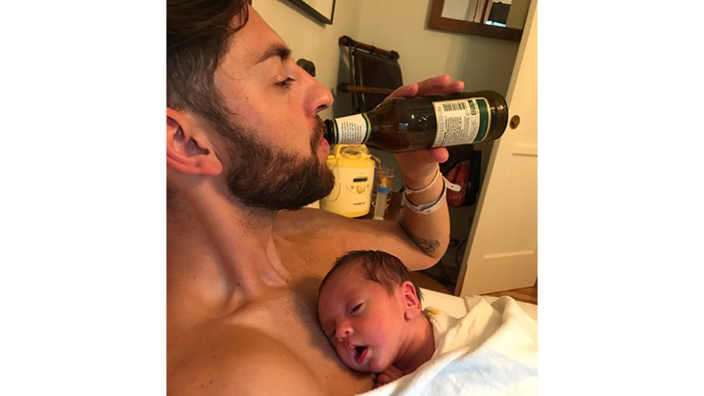 Dad drinking beer while holding his newborn