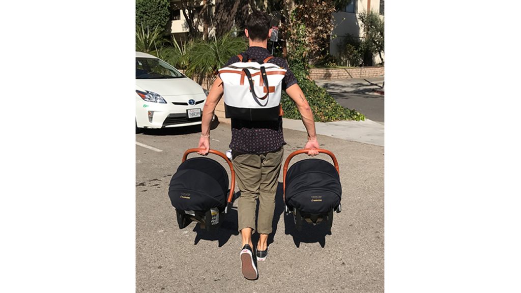 Man Wearing diaper bag backpack and carrying two bucket seats