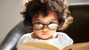 A cute little girl wearing glasses and reading a book