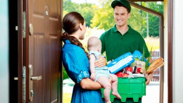 A man is delivery groceries to a woman holding a baby.