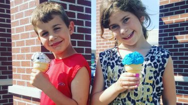 Two kids smiling at the camera while holding ice cream cones