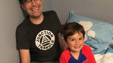 A man and a little boy smiling while sitting on a bed