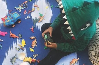 A little boy sitting on the ground playing with dinosaurs