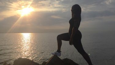 Serena Williams standing on a rock near the ocean silhouetted against a sunrise