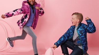 Photo of two kids in puffers kicking a football with a pink background