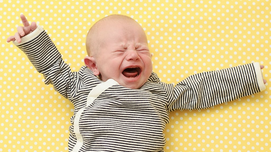 Newborn in a onesie crying with his arms out