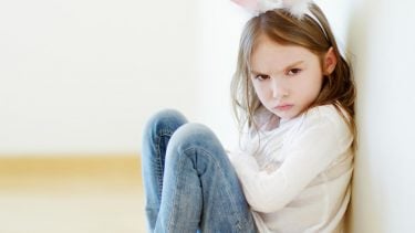 Little girl wearing bunny ears sitting on the floor with her arms crossed