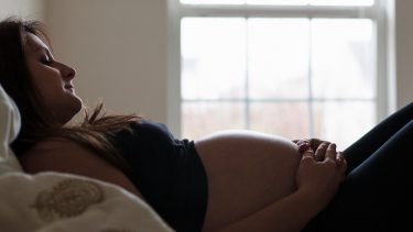 A pregnant woman lying down on the bed holding her belly