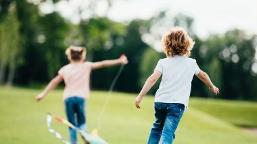 two kids running in a field with a kite