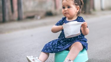 toddler girl sitting on a potty on the street holding toilet paper