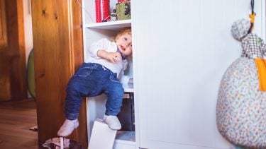A toddler climbing into a cupboard