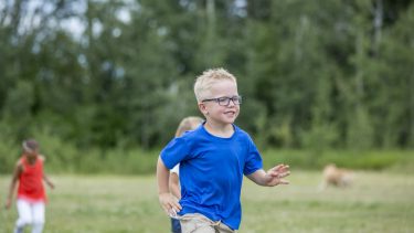 Little boy wearing glasses running in a field