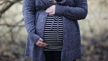 A pregnant woman in a blue sweater standing outside holding her belly