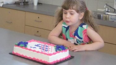 A little girl with pigtails blowing out her birthday cake