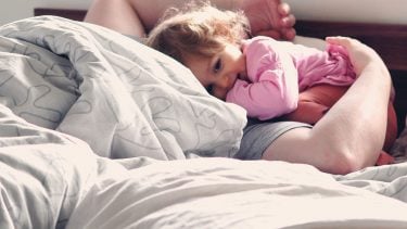 A toddler girl waking her dad up in bed