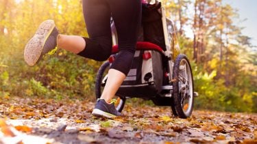 Unrecognizable young mother with her daughter in jogging stroller running outside in autumn nature