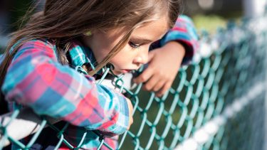 kid leaning on a chain link fence looking sad