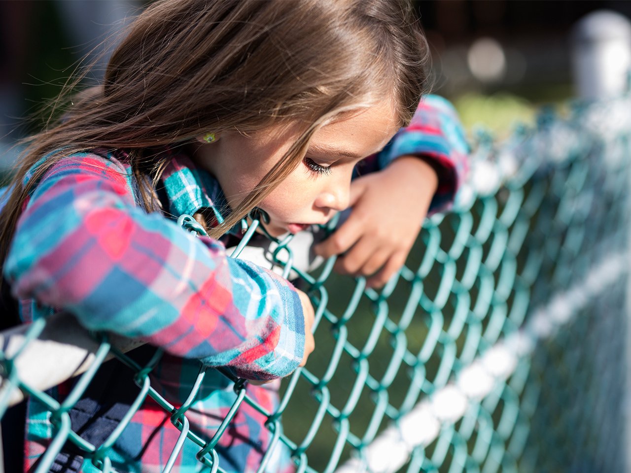 kid leaning on a chain link fence looking sad