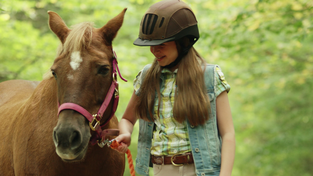 Promo image for Ponysitters Club showing a little girl leading a pony through the forest