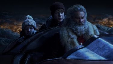 Promo image for The Christmas Chronicles showing two kids riding through the night sky with Santa