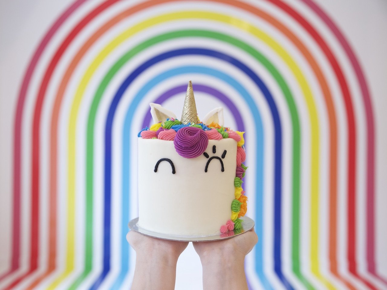 someone holding up a unicorn cake in front of a rainbow