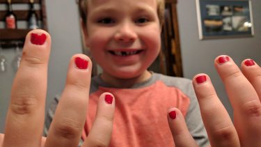 Little boy showing off his fingers with bright red nail polish