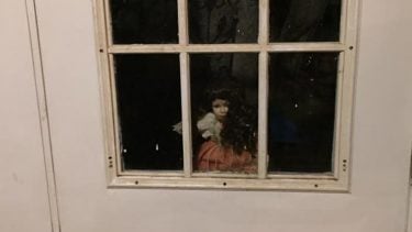 Creepy doll looking through the windows on a door