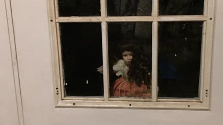 Creepy doll looking through the windows on a door
