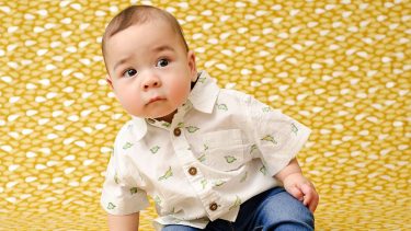 9 month old baby sitting down against yellow background