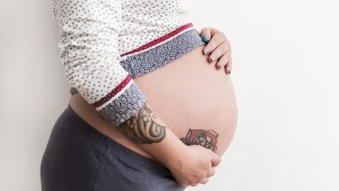 A pregnant woman holding her belly with a tattoo on it
