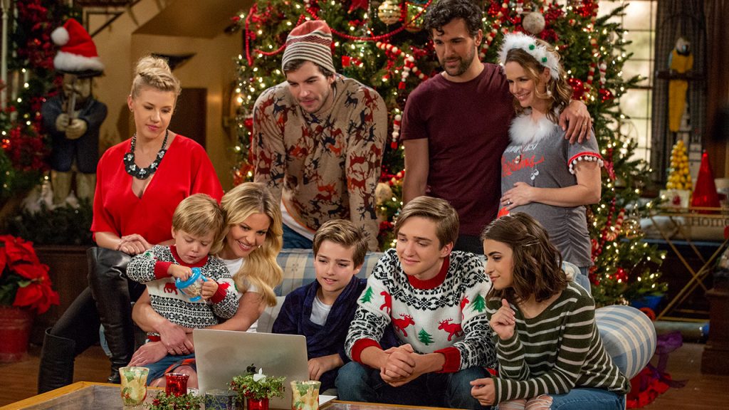 Promo image for Fuller House showing a family gathered on a couch during Christmas watching a video on a laptop