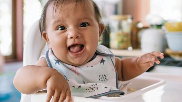Smiling baby sitting in a high chair wearing a bib